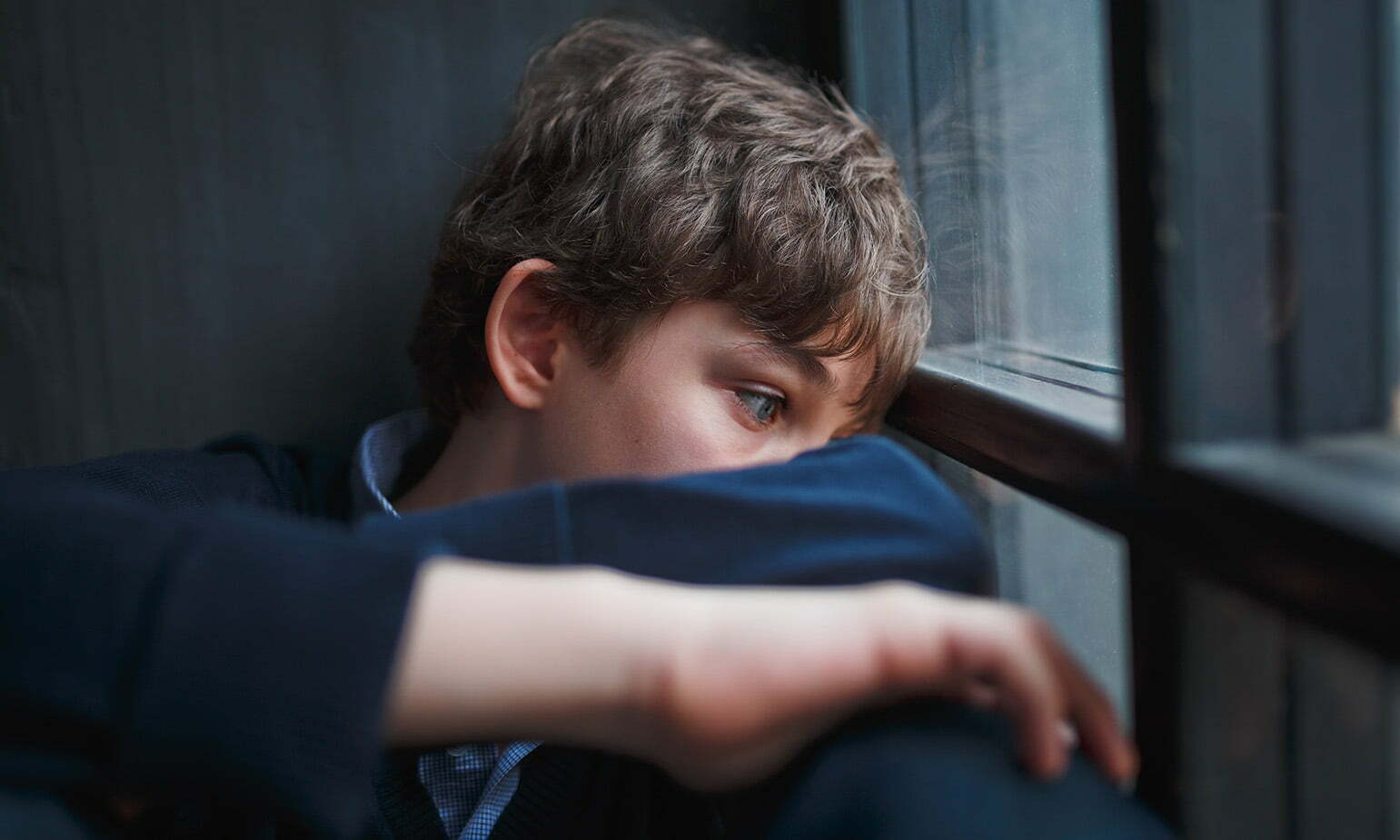 teenaged boy curled up wide eyes staring out window